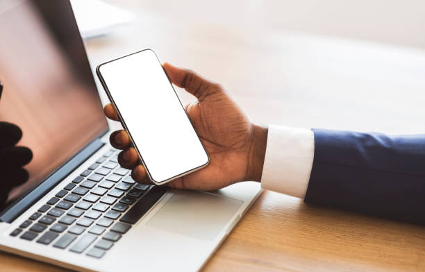 istock Businessman holding smartphone with blank screen and working on laptop 1181591372