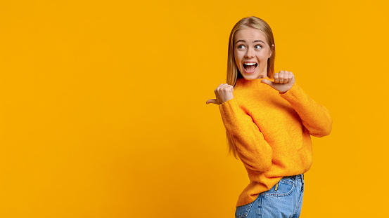 Cheerful cute girl pointing on copy space behing her back with thumbs, panorama with copy space