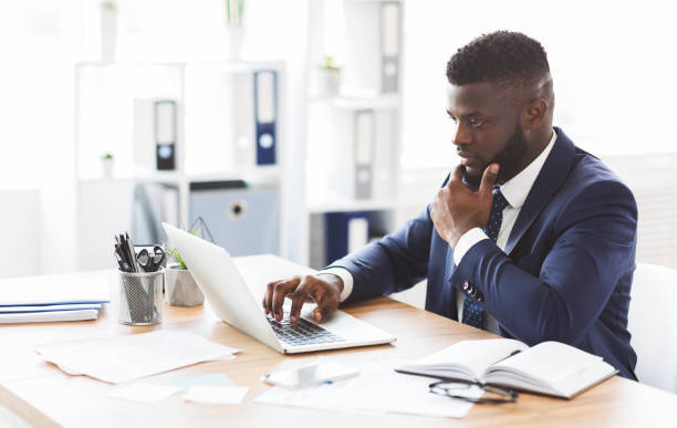 Young afro entrepreneur studying competitors online, using laptop in office, panorama with copy space