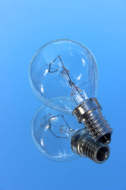 istock Image of clear glass, incandescent light bulb, reflection / reflectiing mirror, blue sky background 1181596023