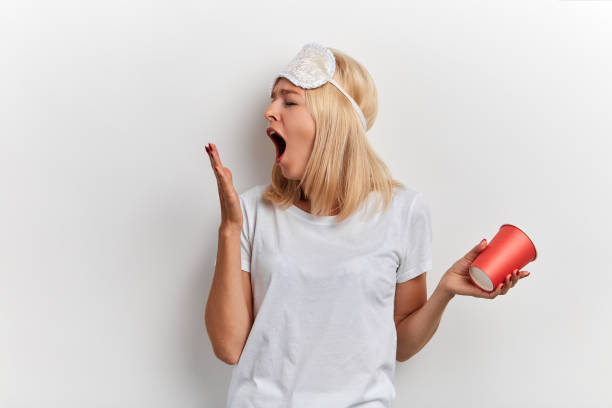 giovane donna stanca con una maschera del sonno sulla testa - yawning women drink coffee cup foto e immagini stock