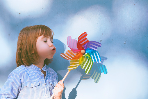 Cute child with rainbow pinwheel toy in front of gray wall. Retro style.