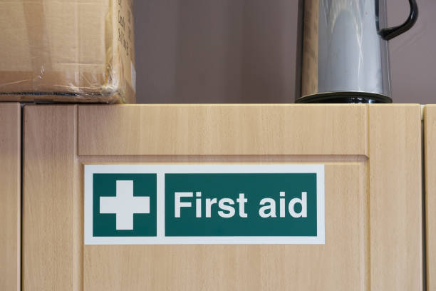 First Aid sign located on an office kitchen cupboard, containing a first aid kit needed by UK law. stock photo