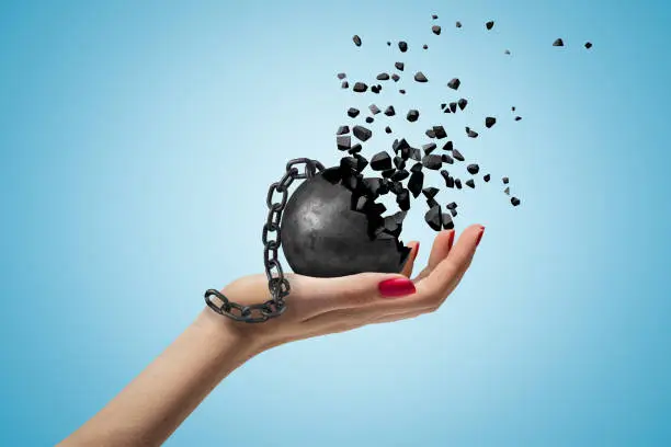 Photo of Closeup of woman's hand facing up and holding black wall and chain dissolving into pieces, on light-blue background.