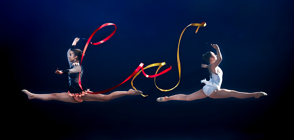 Female gymnasts performing with ribbons against blue background.