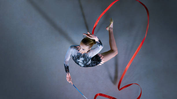 Gymnast performing with ribbon Overhead view of female gymnast performing with ribbon against grey background. leotard stock pictures, royalty-free photos & images