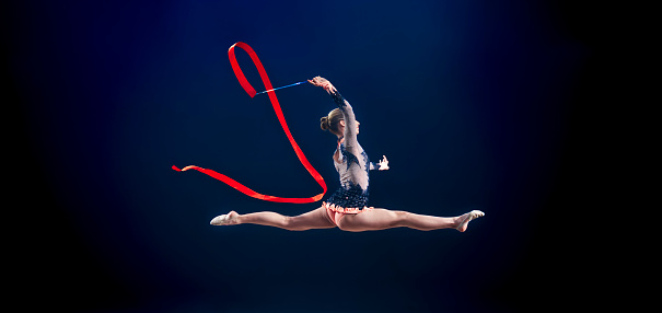 Female gymnast performing with ribbon against blue background.
