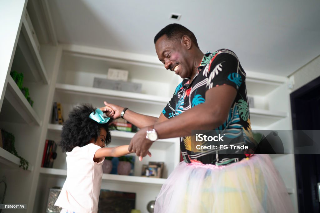 Funny grandfather with tutu skirts dancing like ballerinas with grand daughter Grandfather Stock Photo
