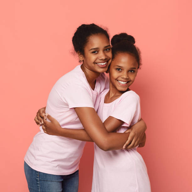 istock Two african girlfriends cuddling over pink background 1181608793