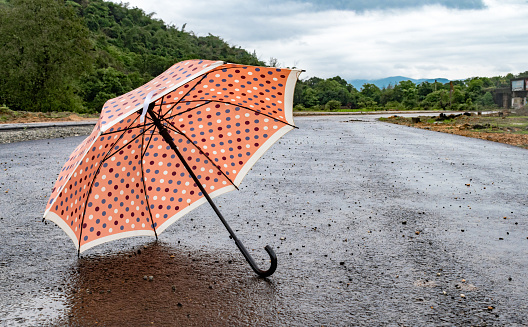Hermoso paraguas que tiene lunares en él, está acostado en un camino vacío en la temporada de lluvias del sur de la India tropical. El clima es muy agradable y exuberantes montañas verdes en el fondo con cielo nublado. photo
