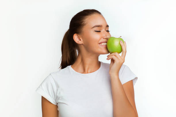 istock Cheerful Girl Eating Apple Standing Over White Background 1181609263