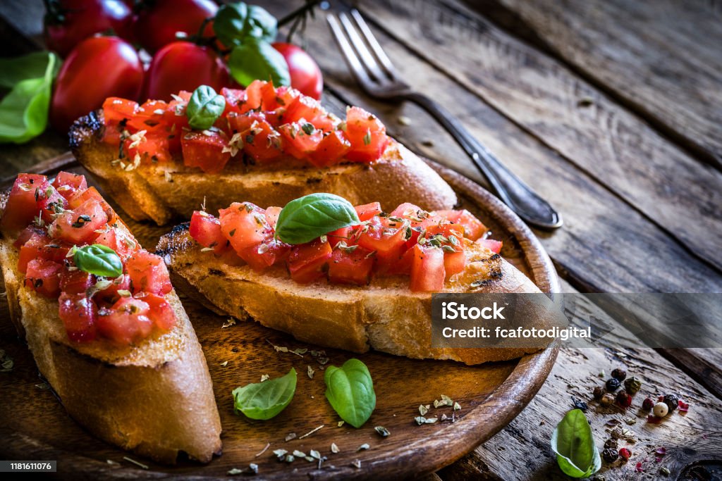 Homemade Italian bruschetta on rustic wooden table Italian food: homemade bruschetta ready to eat shot on rustic wooden table. Olive oil, tomatoes and peppercorns complete the composition. Predominant colors are red and brown. XXXL 42Mp studio photo taken with Sony A7rii and Sony FE 90mm f2.8 macro G OSS lens Bruschetta Stock Photo
