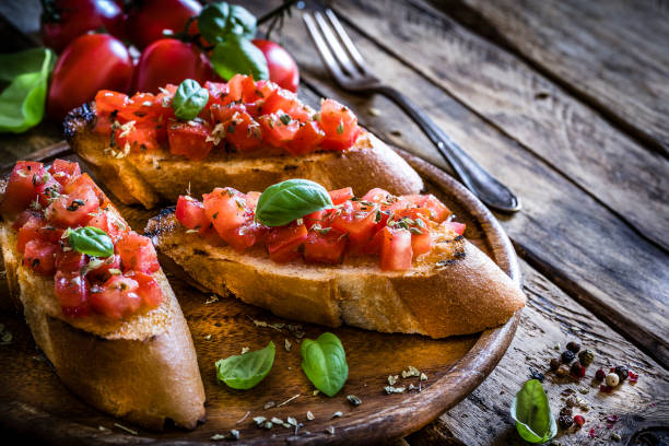 Homemade Italian bruschetta on rustic wooden table Italian food: homemade bruschetta ready to eat shot on rustic wooden table. Olive oil, tomatoes and peppercorns complete the composition. Predominant colors are red and brown. XXXL 42Mp studio photo taken with Sony A7rii and Sony FE 90mm f2.8 macro G OSS lens basil photos stock pictures, royalty-free photos & images