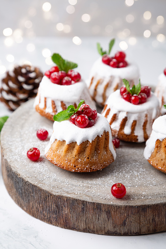 Small Christmas bundt cakes with sugar glaze and  currants on a rustic wood slice with Christmas lights on the background