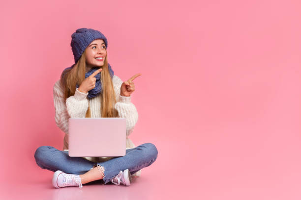 istock Girl with laptop on her lap pointing at empty space 1181611370