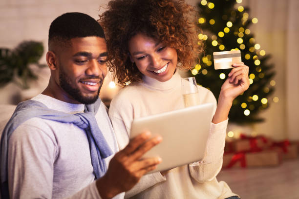 préparation de noel. couples noirs heureux achetant des cadeaux en ligne - ipad shopping gift retail photos et images de collection