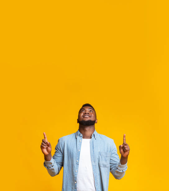 istock Black guy pointing upwards at copy space on yellow background 1181611598