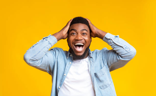 Amazed man holding hands on head and looking at camera Wow. Excited african american guy holding hands on head, looking at camera with amazement, yellow studio background facial expression surprise stock pictures, royalty-free photos & images