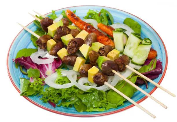 Fried shish-kebab from chicken hearts with  avocado and  fresh lettuce served at plateï»¿. Isolated over white background