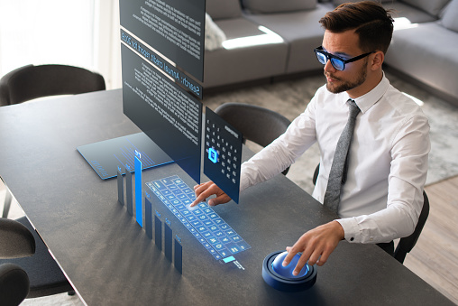 Young businessman working from home. He is using Augmented Reality glasses and the entire interface he sees is on the above the table.