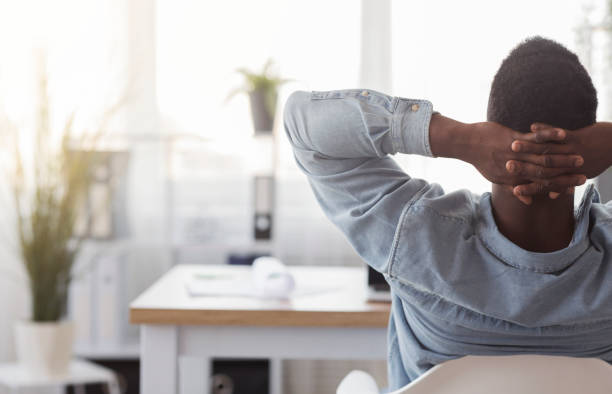 istock Black worker sitting in office with hands behind his head 1181621690