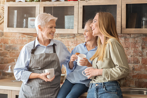 Female family drinking tea and talking, mom, daughter and granny spending time together at kitchen, copy space