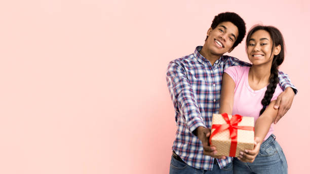 istock Joyful afro couple holding gift box and stretching to camera 1181624419