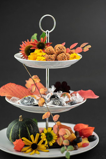 Studio shot of a cake stand with truffles / rumkugler / brigadeiros orange sprinkled together with candy and season’s flowers, leaves and a pumpkin.

The background is black.