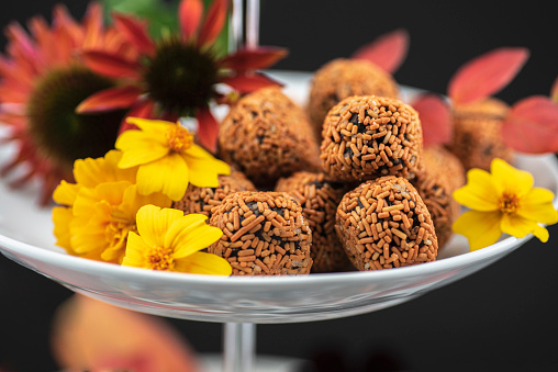 Studio shot of truffles / rumkugler / brigadeiros orange sprinkled together with red coneflowers and marigolds.

The background is black.