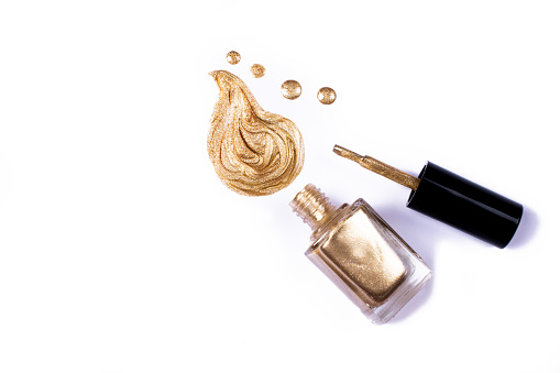 Golden glitter nail polish drops and strokes as samples, bottle and brush isolated on white background with copy space for text. Beauty, fashion and woman lifestyle concept.