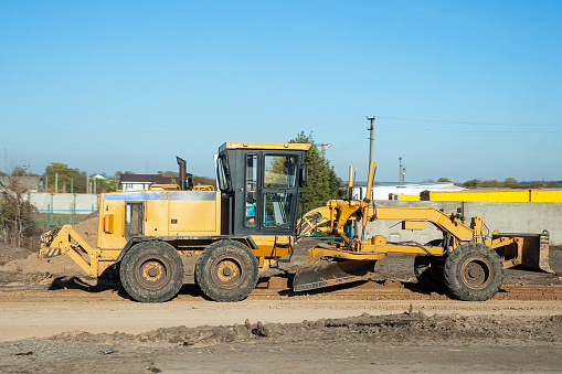 Yellow grader stands on the road outside the city. A machine for planning and profiling areas and slopes, leveling and moving soil or bulk building materials. Road work on an intercity highway
