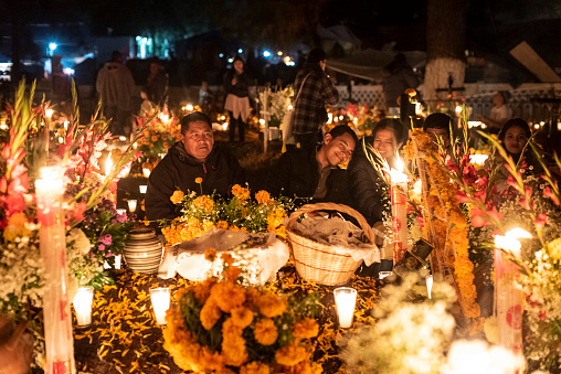 Tzintzuntzan, 02/11/2018: Family gathered in front of a tomb in the cemetery located in Tzintzuntzan in the region of Patzcuaro, in the Mexican state of Michoacan. On November 1st and 2nd, the local community gathers in the cemetery to celebrate Day of the Dead, when, according to Mexican belief, the souls of the dead return to visit their families. During the celebration the tombs are adorned with flowers, candles and the favorite foods of the deceased as a way to welcome their souls in a joyful way.