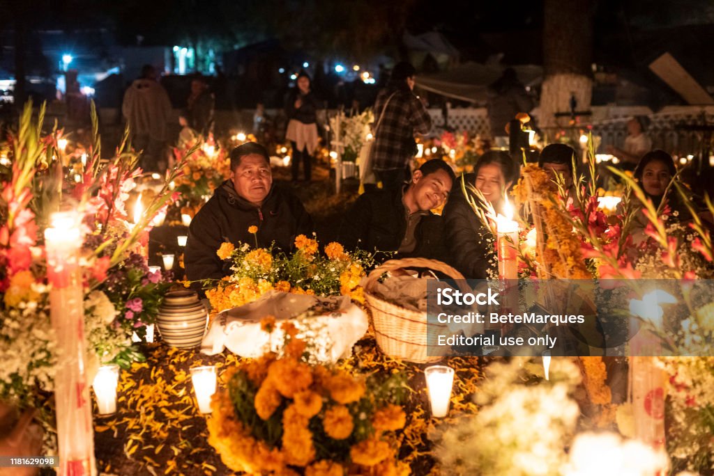 Celebration of Mexican Day of the Dead at Tzintzuntzan Cemetery in the Pátzcuaro Region of Michoacán State. Tzintzuntzan, 02/11/2018: Family gathered in front of a tomb in the cemetery located in Tzintzuntzan in the region of Patzcuaro, in the Mexican state of Michoacan. On November 1st and 2nd, the local community gathers in the cemetery to celebrate Day of the Dead, when, according to Mexican belief, the souls of the dead return to visit their families. During the celebration the tombs are adorned with flowers, candles and the favorite foods of the deceased as a way to welcome their souls in a joyful way. Day Of The Dead Stock Photo