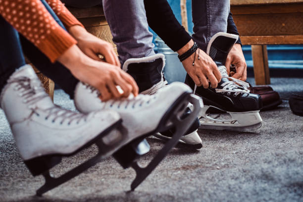 Young couple preparing to a skating. Close-up photo of their hands tying shoelaces of ice hockey skates in the locker room stock photo