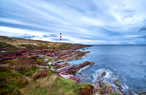 Tarbat Ness a red and white lighthouse, you can see the sea and the rocks in the foreground. It is a cloudy day.