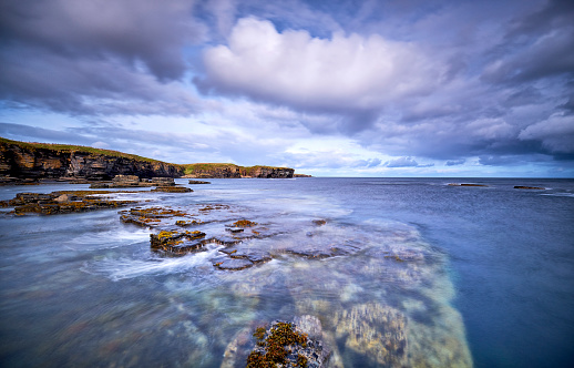 Rock formations along the Scottish coast. The water is so clear that you can see the rocks underwater. A slow shutter speed has been used so that the water is flat and the clouds seem to move.