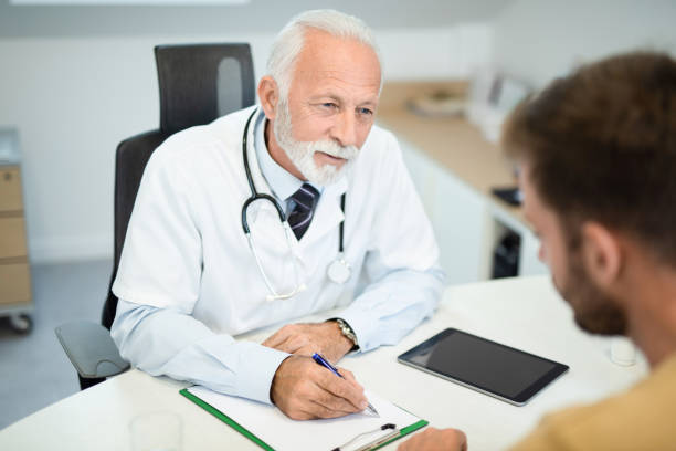 수석 남성 의사는 환자를 듣고 약을 처방합니다. - doctor male doctor mature men portrait 뉴스 사진 이미지
