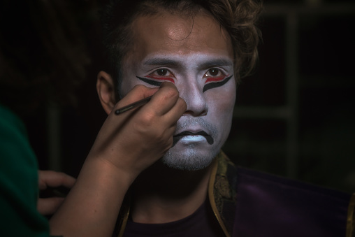 japanese taiko artist man puts makeup on face in the form of a demon mask, close up portrait