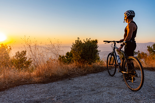 Male biker watching the sunset while resting after ride - training