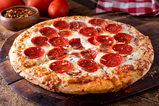 A delicious brick oven baked pepperoni pizza on a rustic wood serving board.