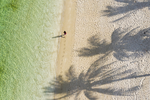 Female walking along perfect beach with palms and clear water, early morning Rote Island, Indonesia
