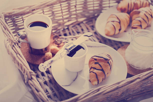 Breakfast Continental  with Fresh  Croissants on a  white Background  wicker tray Breakfast in bed. Coffee with Milk and Delicious Baking with  with Chocolate Topping Toned image Vintage style