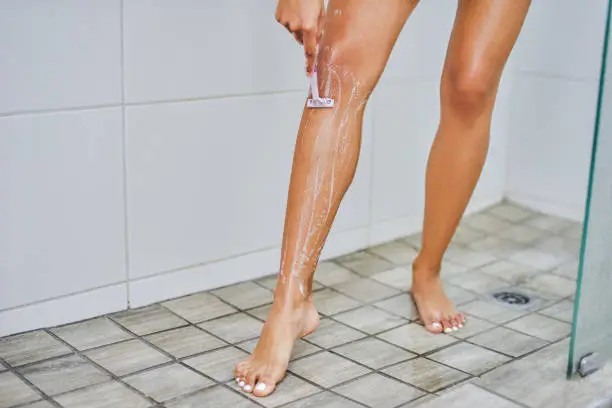 Cropped shot of an unrecognizable woman shaving her legs with a razor inside the shower at home
