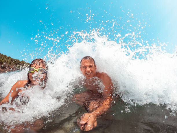 istock Father and daughter getting splashed by the sea wave 1181655557