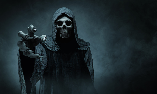 Grim reaper reaching towards the camera over dark misty background with copy space