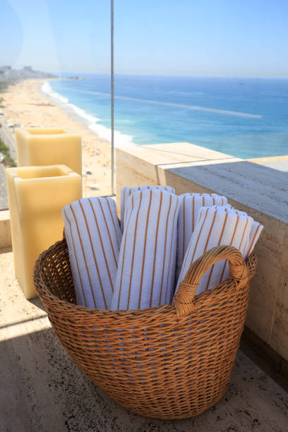 Towel Bale in a wicker basket with the beach in the background Roof top view through a picture window of Copacabana Beach, Brazil  with a wicker basket with clean white and brown stripped towels with large candles in the background. moses basket stock pictures, royalty-free photos & images