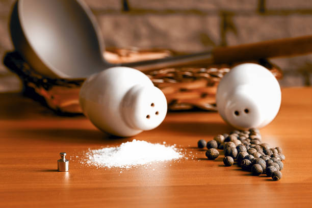 On the kitchen table there is a weight weighing two grams displaying the necessary amount of salt and pepper not yet ground scattered next to the salt and pepper shaker.