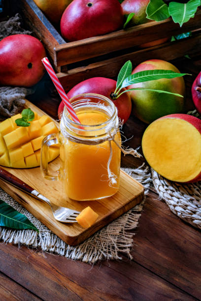 Mango smoothie juice and fruit un drinking glass on wooden table in rustic kitchen