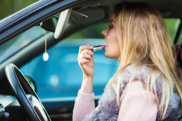 istock Young woman applying lipstick in car 1181666874
