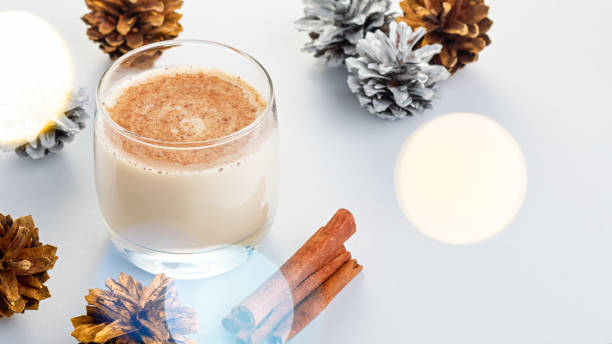 cocktail tradizionale natalizio eggnog con uova, alcol, noce moscata grattugiata e primo piano alla cannella. bevanda dolce tradizionale su tavolo grigio con decorazioni beige e pigne - luxury milk dinner glass foto e immagini stock